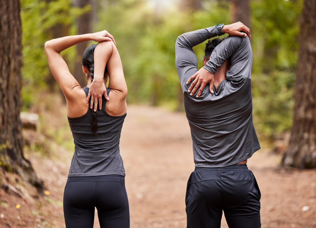 Back, fitness and stretching with couple in forest for start of marathon, training or workout. Exercise, health and warm up with athlete or runner people in nature for cardio preparation together.